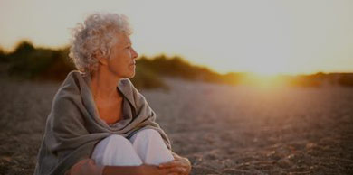 Old woman watching the sun set on the beach