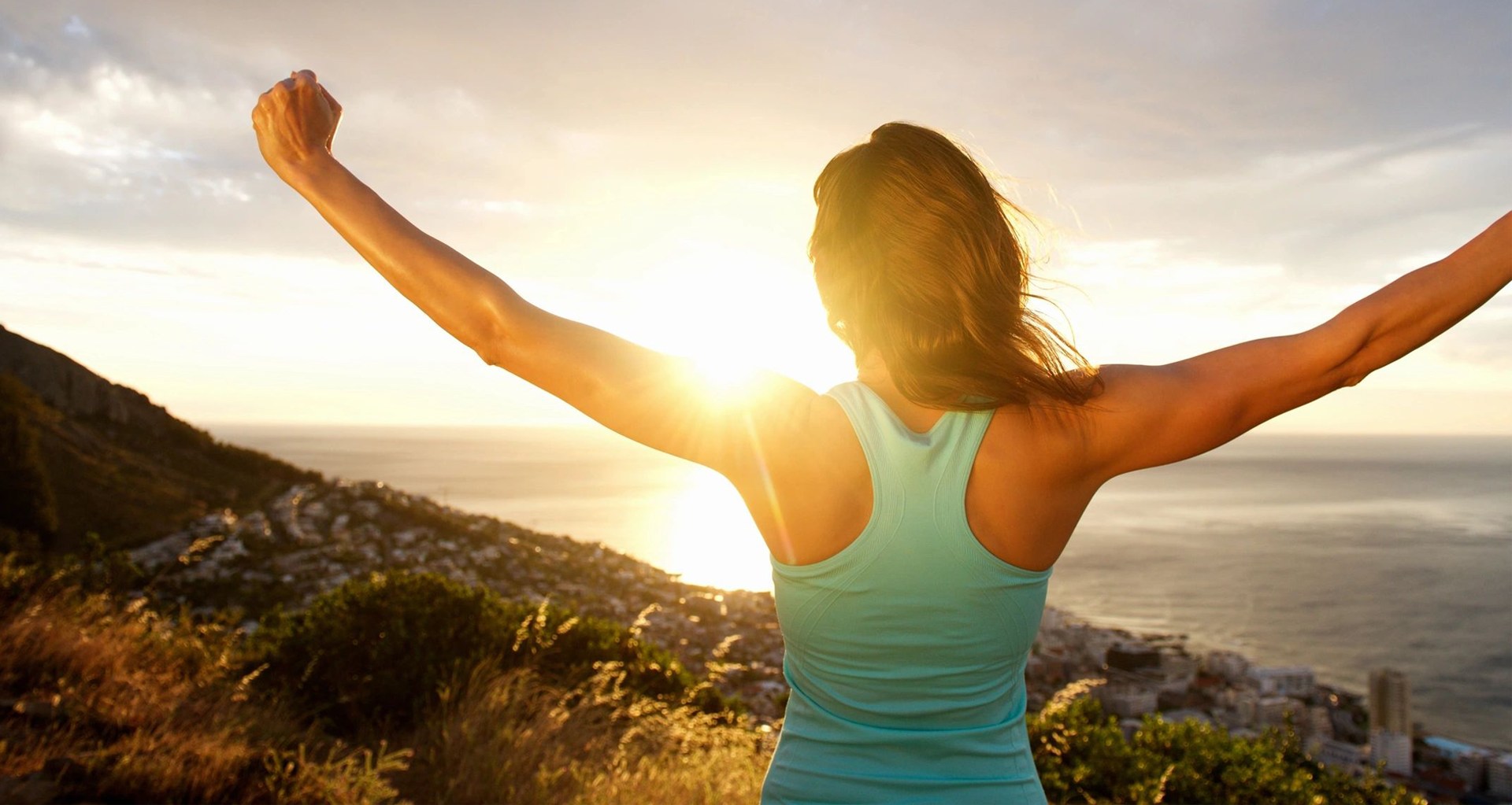 woman stretching out her arms in front of sunrise